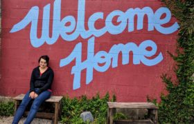 Girl sitting in front of a sign that says "Welcome Home"