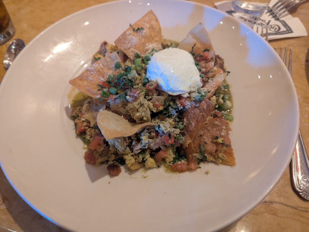 A big white bowl with seven chips, a blob of sour cream, and crumbly eggs.